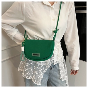 Detail of green saddle bag with knit texture, Merrey brand tag and knotted shoulder strap