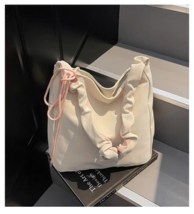 Detail view of a cream-white tote bag with pleated straps resting on books over gray steps