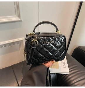 Vue détaillée de la texture en cuir noir matelassé et du logo en métal doré du sac à main