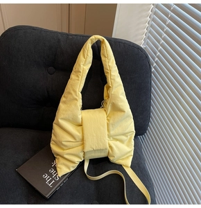 Macro detail of yellow quilted bow shoulder bag with padded texture on a dark sofa