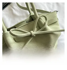 Gros plan détaillé du cuir vert clair avec nœud et coutures de précision sur le sac à main