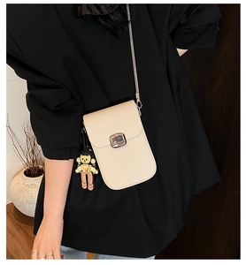 Close-up of beige lychee leather crossbody phone bag with metal buckle and girl charm