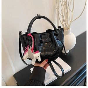 Close-up of black crocodile pattern leather bucket bag with a white Pegasus charm accessory