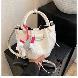 Detail of white crocodile pattern bucket bag with round handle and pony charm accent