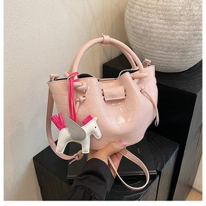 Detail of light pink crocodile pattern bucket bag with a decorative Pegasus horse charm
