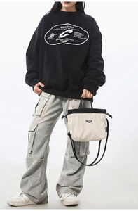 Detail of off-white and black drawstring crossbody bag held by a casual model