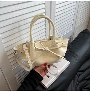 Détail du sac à main crème avec nœud décoratif, texture grainée et finitions argentées
