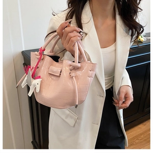 Detail of light pink crocodile pattern bucket bag with a decorative white horse charm