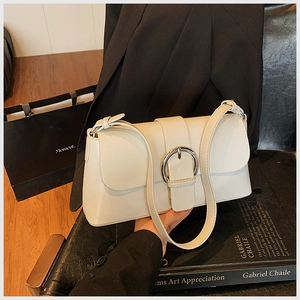 Detail of a creamy beige leather baguette bag with a polished silver circular metal buckle