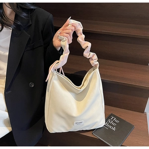 Detail of soft cream tote bag featuring multi-colored pleated shoulder strap and brand label