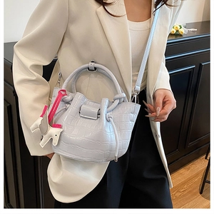 Detail of light blue croc-embossed bucket bag with cute white horse charm and strap