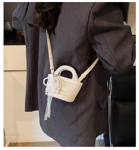 Detail view of a white mini bucket bag with litchi grain texture and lace pearl charm