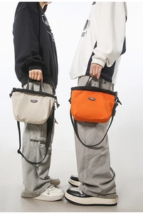 Detail view of nylon drawstring crossbody bags in beige and orange with brand logo and strap