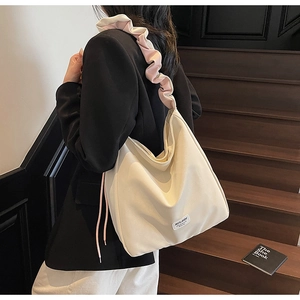 Detail of cream tote bag with pink ruffled strap worn by a model on wooden stairs