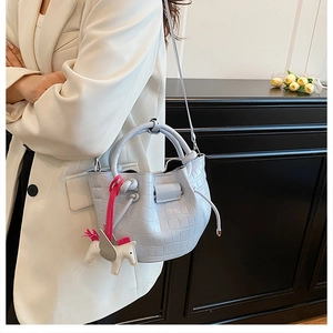 Detail of light blue faux leather bucket bag with crocodile texture and horse charm