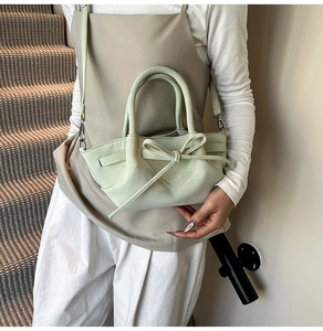Détail d'un sac seau en cuir vert menthe avec un nœud décoratif et des clips en métal argenté