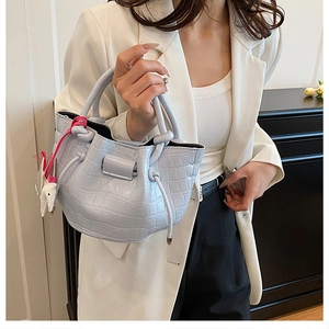 Detail of light blue faux leather bucket bag with crocodile texture and horse charm