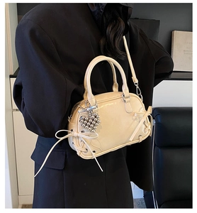 Beigefarbene Boston-Tasche mit Schleifen-Details und Herzanhänger auf schwarzem Blazer