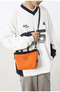 Detail of orange drawstring crossbody bag with logo patch and durable nylon texture