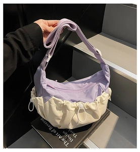 Detail of color-block crescent bag with drawstring base and wide purple strap on books