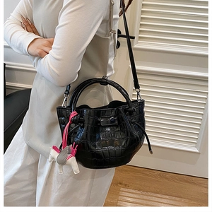 Detail shot of black crocodile-embossed bucket bag with metallic ring handle and horse charm
