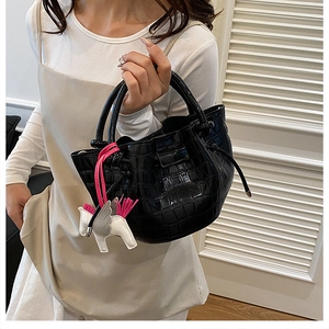 Detail of black faux leather bucket bag with crocodile texture and winged horse charm