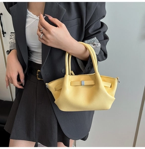 Détail d'un sac à main jaune en cuir avec fermoir argenté porté sur un tailleur gris
