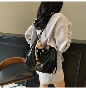 Détail du sac hobo en cuir noir souple avec charm lion en peluche et logo embossé