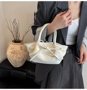 Sac à main crème chic avec nœud et texture cuir grainé porté avec un costume gris