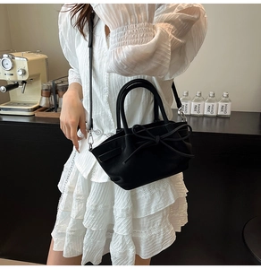 Détail du sac panier en cuir noir avec grand nœud et bandoulière élégante sur le côté