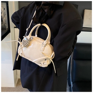 Detail der cremeweißen Boston Bag mit Schleifen und silbernem Herzanhänger am Model
