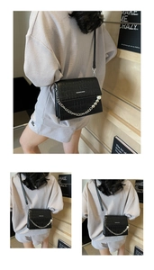 Detail view of black crocodile pattern saddle bag with pearl chain and metal strap