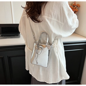 Mini sac argenté métallisé porté par un modèle avec pendentif cœur et bandoulière longue