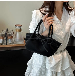 Détail d'un sac à main noir texturé avec nœud décoratif tenu par un mannequin en robe blanche