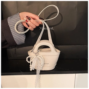 Detail of cream mini bucket bag featuring pebble leather and pearl lace bow charm