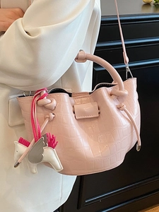 Pink crocodile-textured handbag with a horse charm, carried by a model in a white blazer