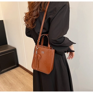 Détail du sac vintage en cuir ciré marron avec texte blanc et accessoire pendentif coeur