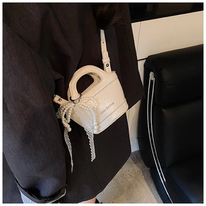 Detail of cream patent leather mini bag with pearl handle and lace ribbon accessory