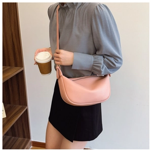 Close-up of pink crescent crossbody bag with silver zipper and pebbled leather texture