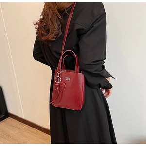 Détail du sac en cuir ciré rouge avec pendentif cœur et logo métallique sur robe noire