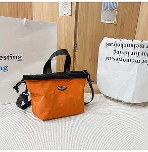 Close-up of bright orange nylon crossbody bag with black drawstring top and logo detail