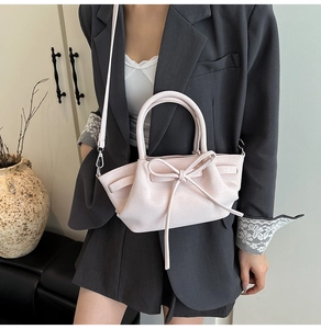 Sac à main rose en cuir grainé avec nœud porté par un mannequin en veste grise