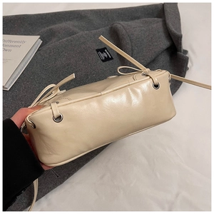 Detailansicht der cremefarbenen Ledertasche mit Metallösen und Schleifenakzenten