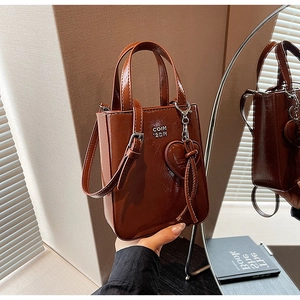 Détail de sac à main en cuir marron glacé avec logo métallique et breloque cœur