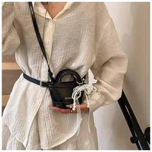 Detail of mini black patent leather bucket bag with white lace bow and pearl tassel decor
