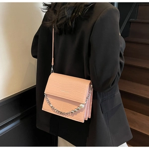 Close-up of pink croc-effect crossbody bag with silver chain and pearl detail on model