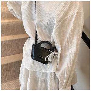 Detail shot of mini black crossbody bag featuring a pearl charm and lace bow on a model