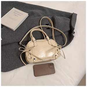 Detail der cremefarbenen Boston Bag mit Metallösen, Schleifen und Gurt auf einem Mantel
