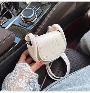 Détail du mini sac selle crème avec ours en relief et lettrage élégant sur le rabat