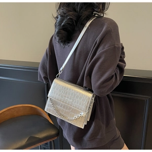 Close-up of silver crocodile embossed crossbody bag with metallic chain and pearl accents